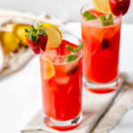 two glasses filled with strawberry lemonade and garnished with mint, fresh strawberries and lemon slices
